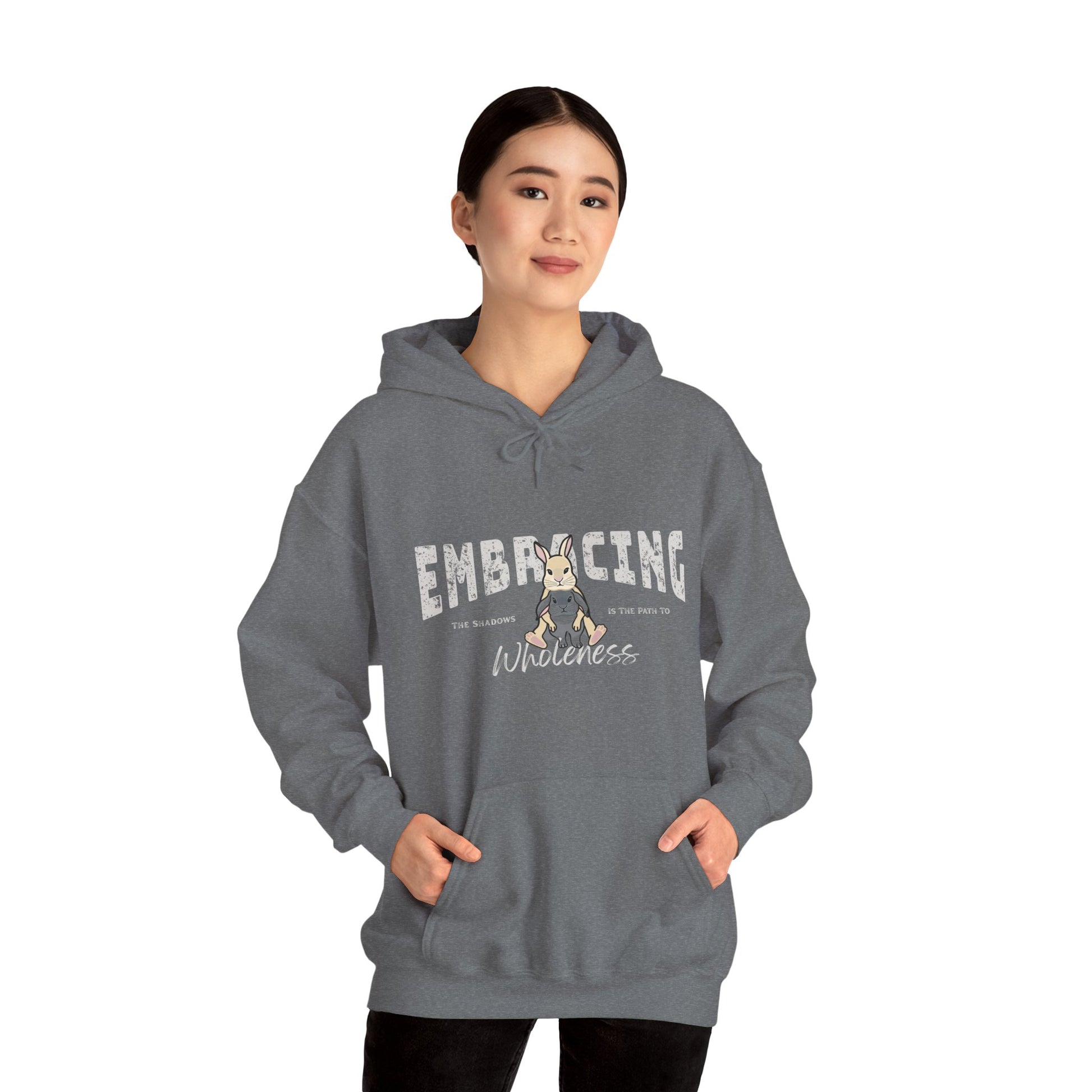 Woman wearing a blue-gray hoodie with a graphic of cream Holland Lop rabbit hugging gray Holland Lop rabbit and text 'Embracing the shadows is the path to wholeness' on a white background