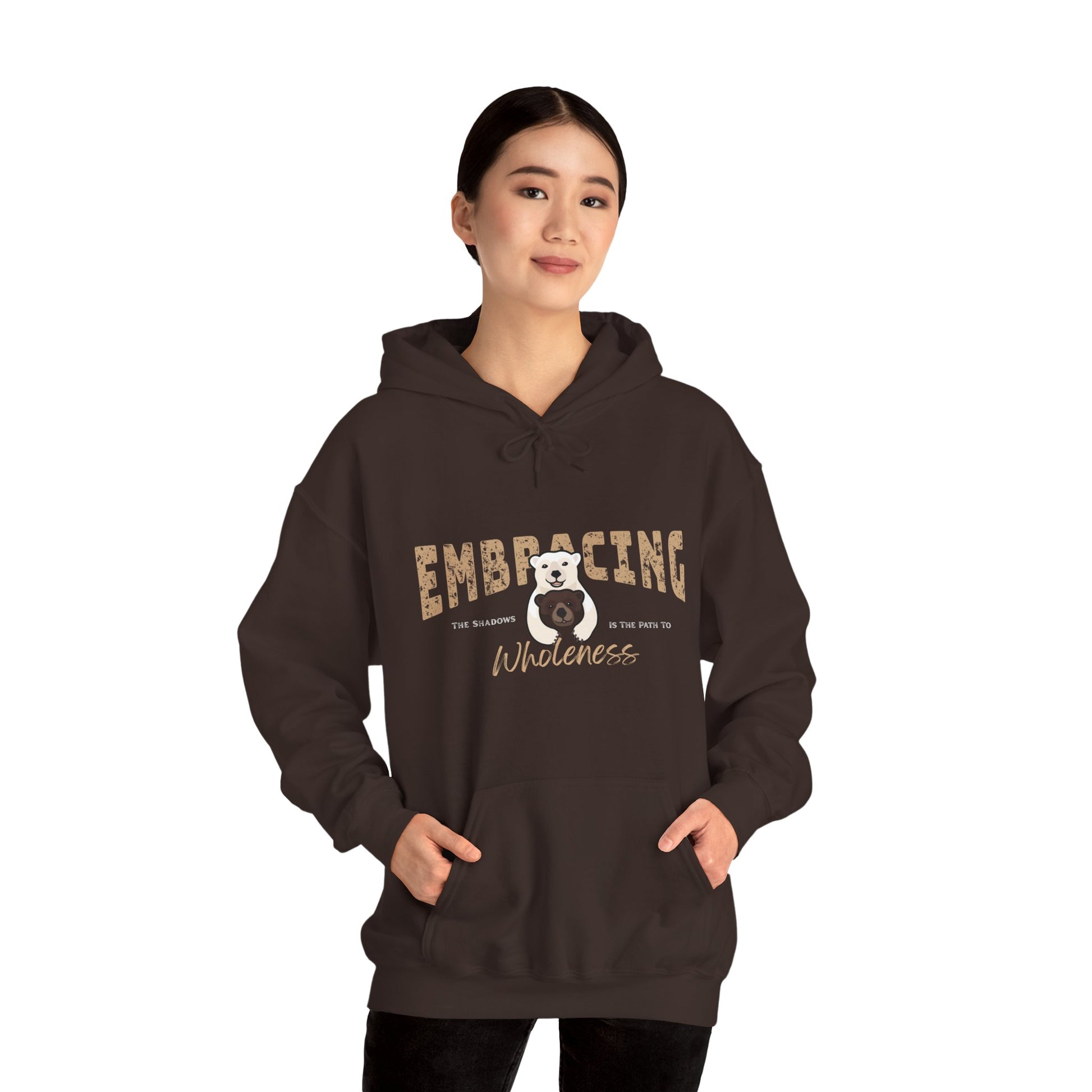 Woman wearing a chocolate brown hoodie with a graphic of polar bear hugging brown bear and text 'Embracing the shadows is the path to wholeness' on a white background