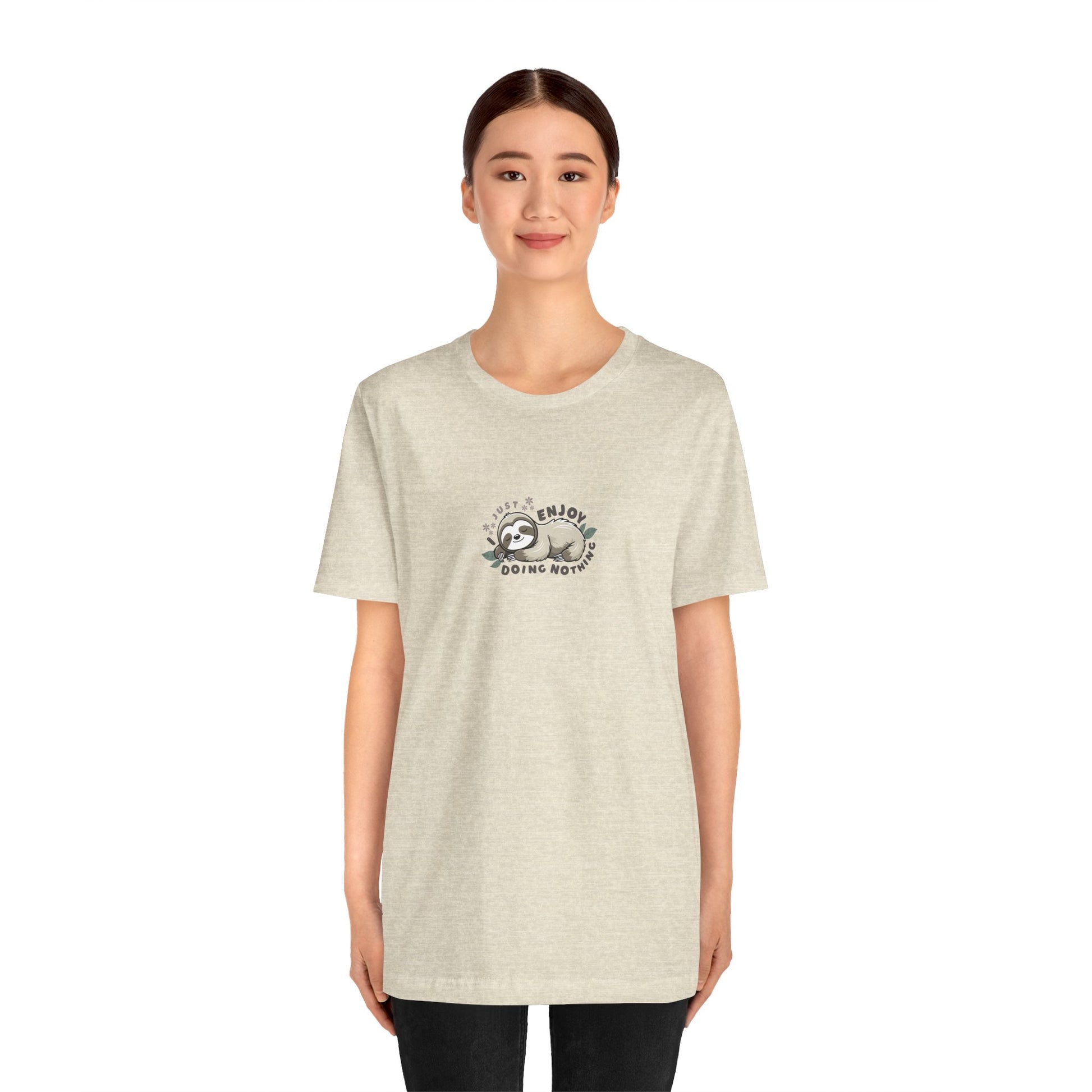 Woman wearing a cream beige t-shirt with a sleeping sloth graphic and text 'I just enjoy doing nothing' on a white background