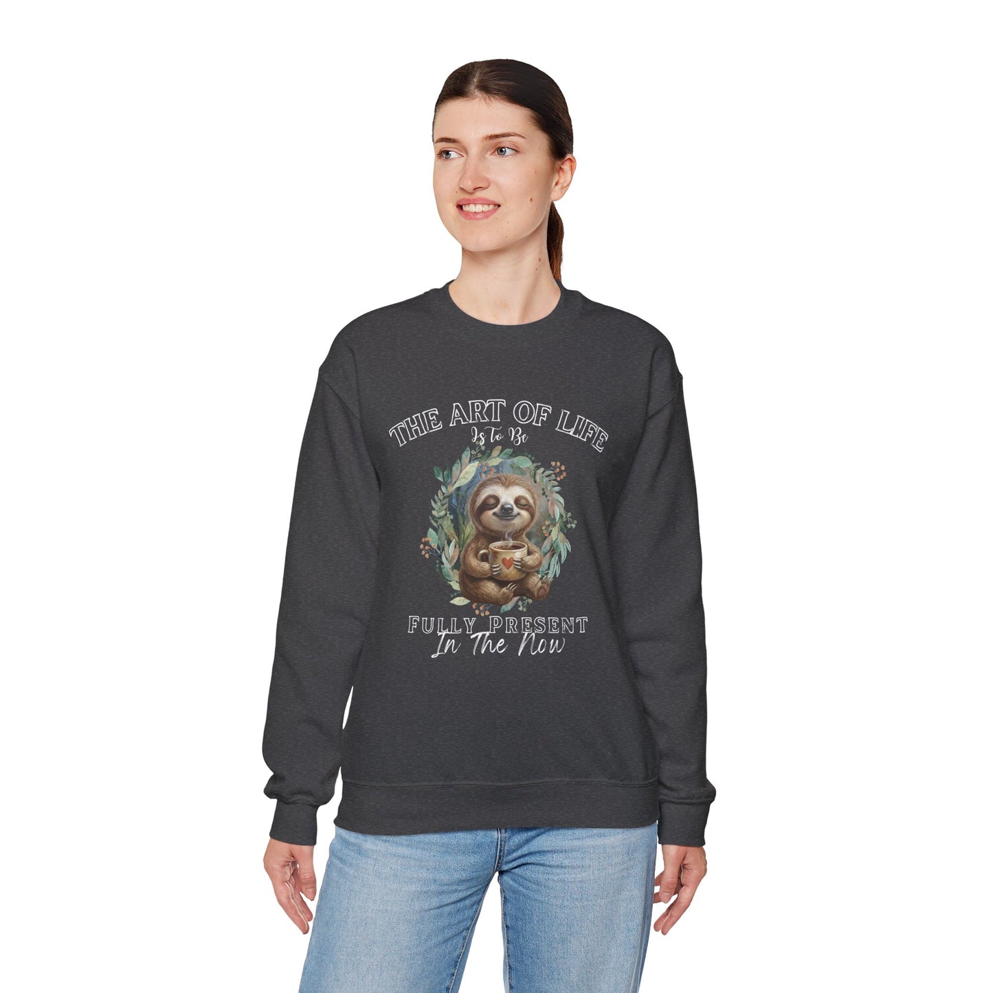 Woman wearing a dark gray sweatshirt with a sloth drinking coffee graphic and text 'The art of life is to be fully present in the now' on a white background