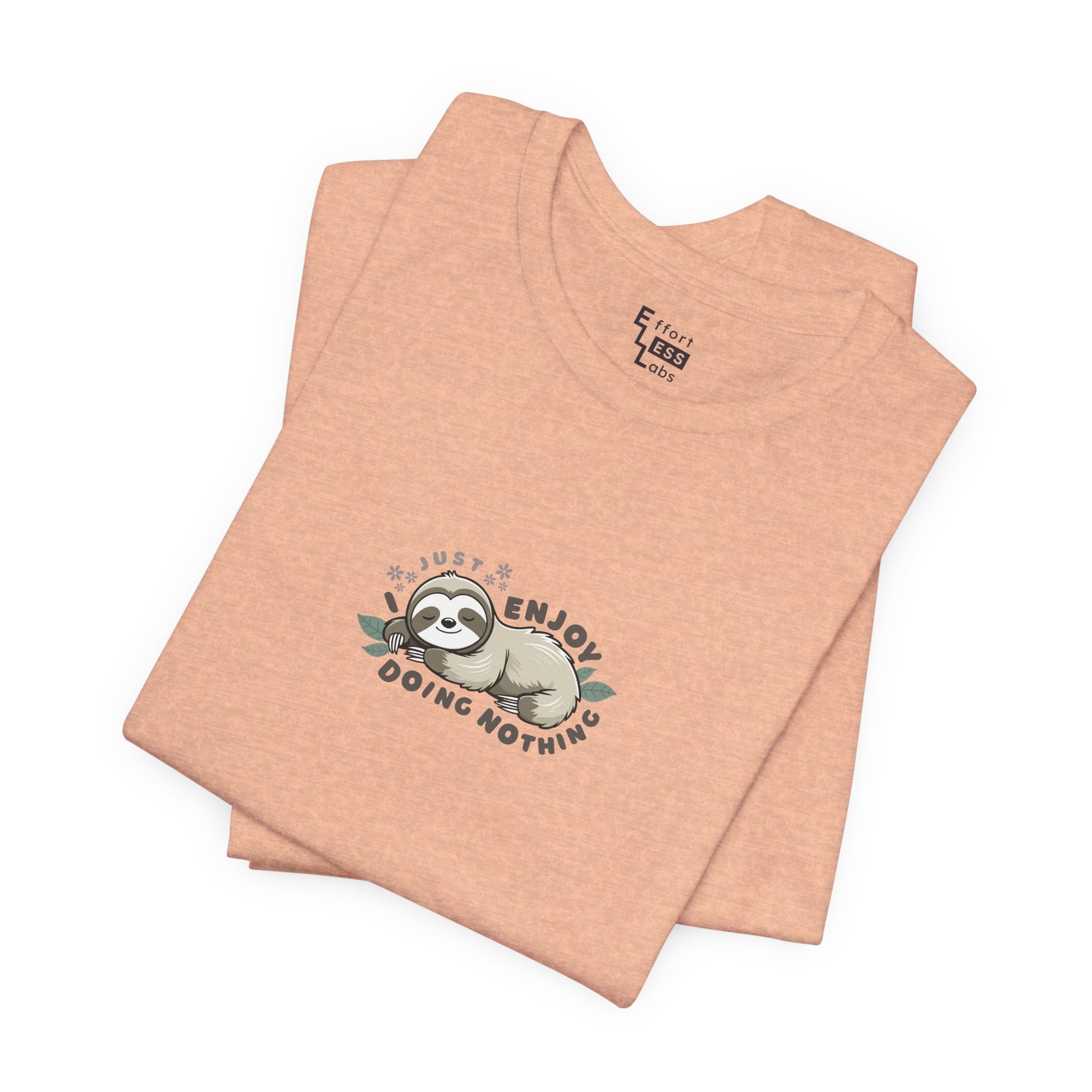 Folded peach-colored t-shirt with a sloth graphic and text 'I just enjoy doing nothing' on a white background