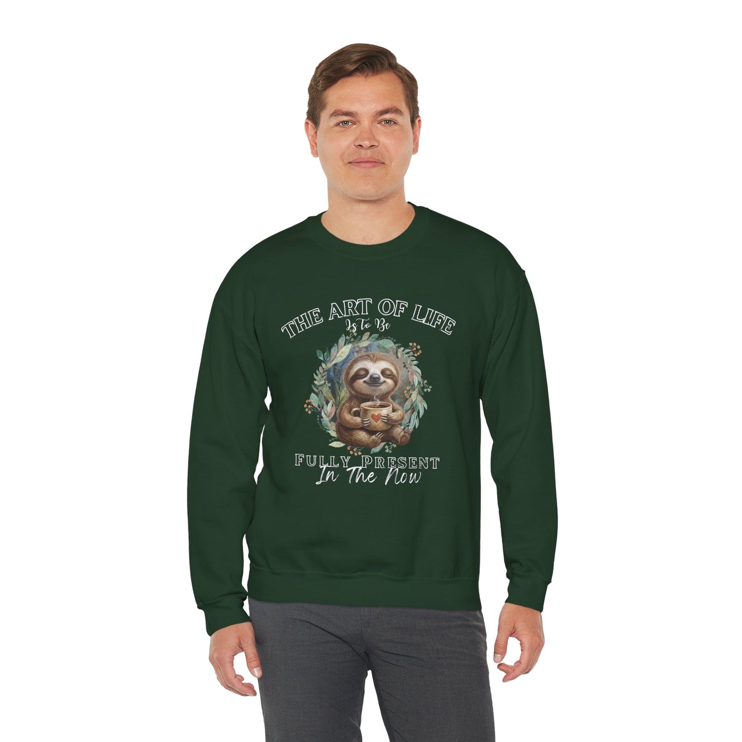 Man wearing a dark green sweatshirt with a sloth drinking tea graphic and text 'The art of life is to be fully present in the now' on a white background