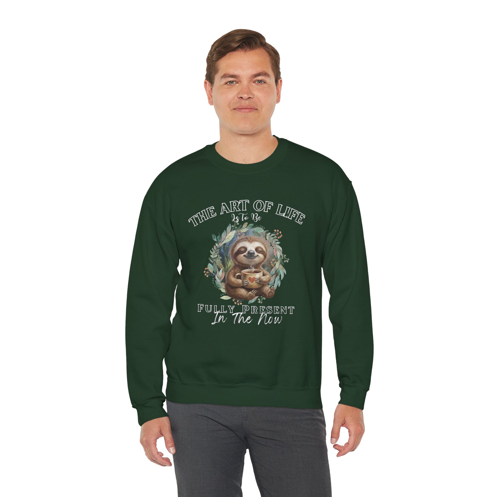 Man wearing a dark green sweatshirt with a sloth drinking tea graphic and text 'The art of life is to be fully present in the now' on a white background