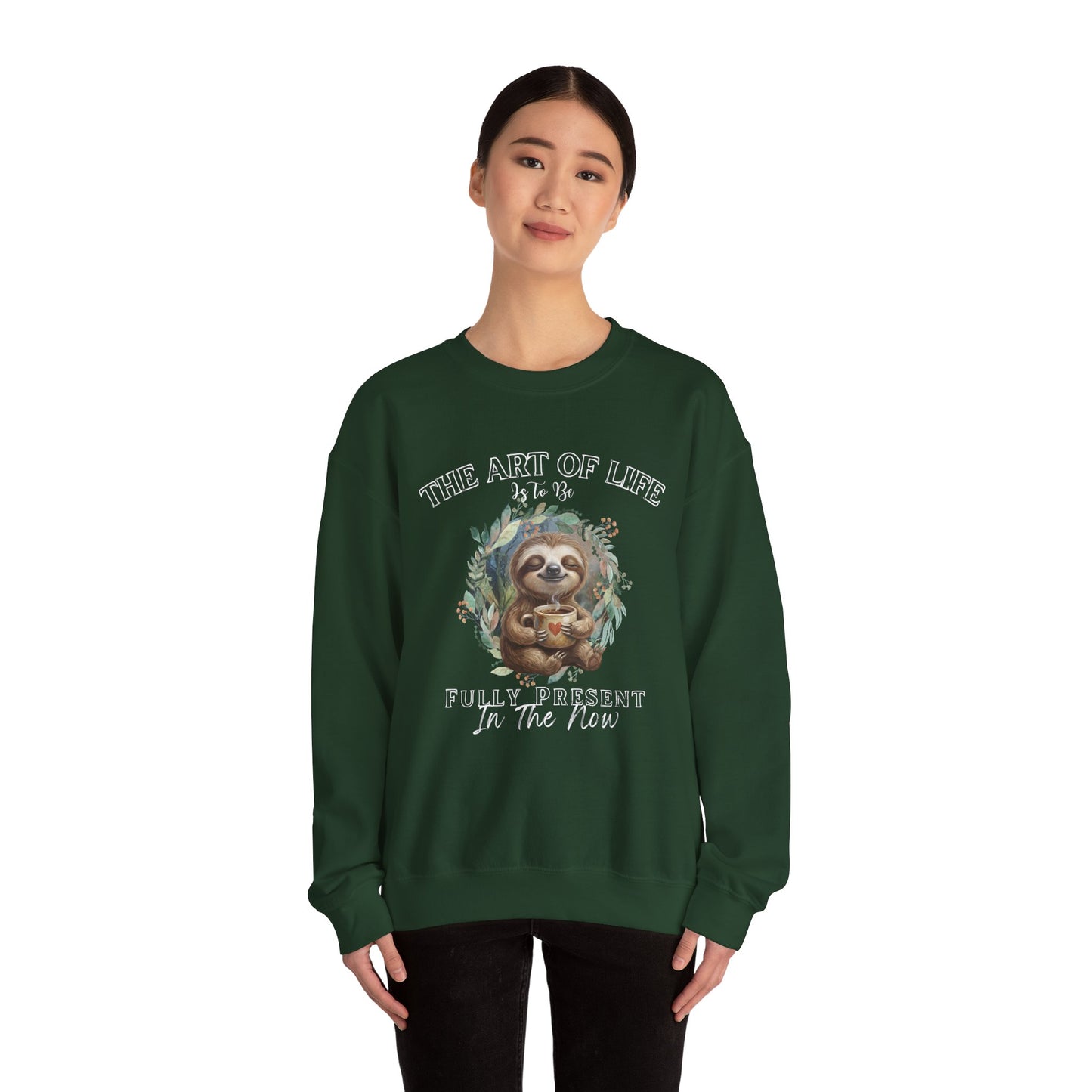 Woman wearing a dark green sweatshirt with a sloth drinking tea graphic and text 'The art of life is to be fully present in the now' on a white background